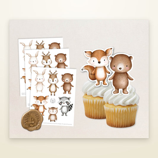 Baby woodland animal cake toppers on printed sheets and standing on two cupcakes