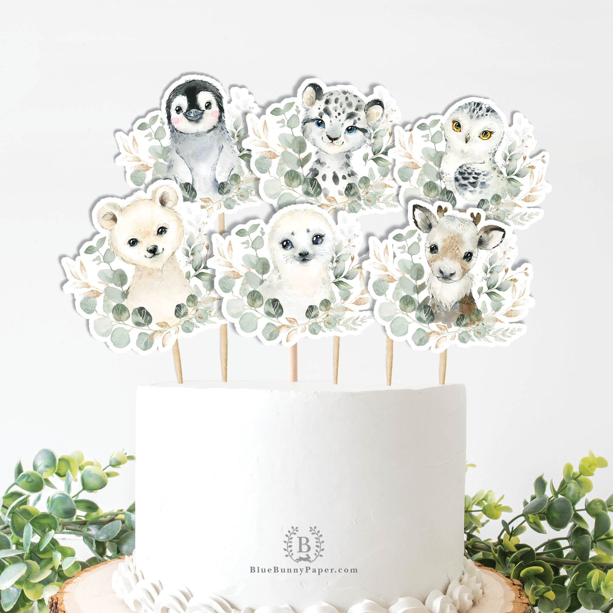 Winter animal cake toppers on a white cake: penguin, snow leopard, owl, polar bear and arctic fox